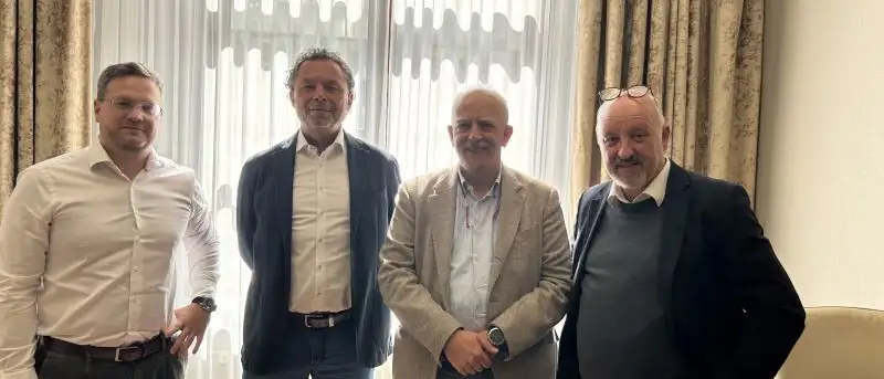 Vier Personen stehen gemeinsam im Raum vor einem großen Fenster.