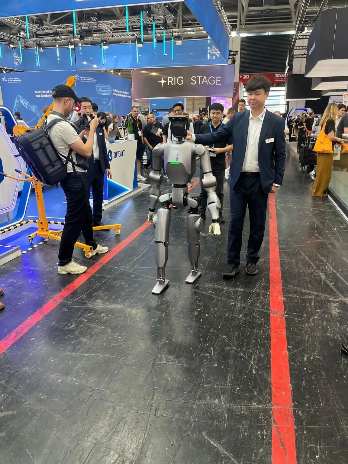 Messeszene mit mehreren Personen und einem humanoiden Roboter auf einem Stand.