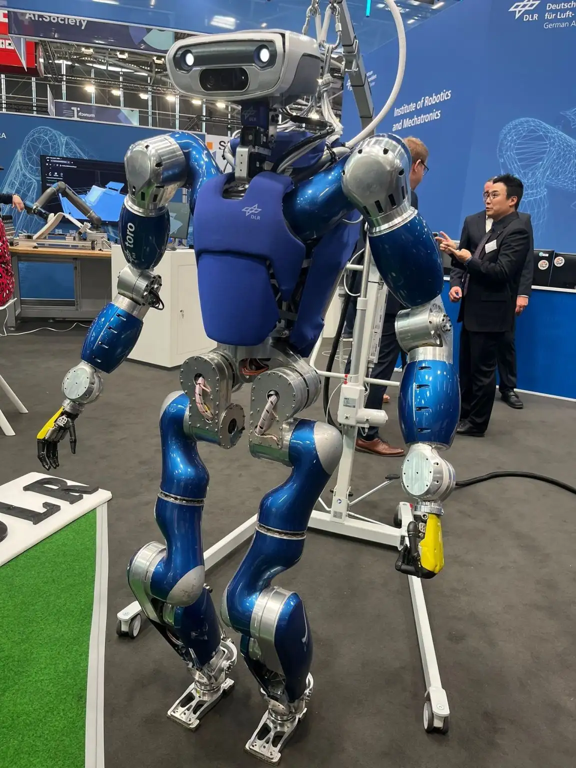 Humanoider Roboter auf einer Messe, umgeben von Gesprächssituationen.