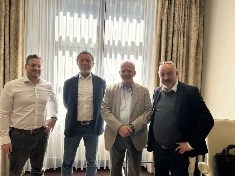 Vier Personen stehen gemeinsam im Raum vor einem großen Fenster.