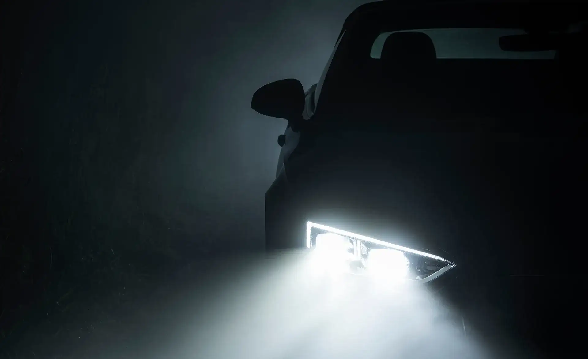 Ein Auto fährt durch dichten Nebel, sichtbar ist nur der rechte Scheinwerfer mit starkem Lichtkegel.