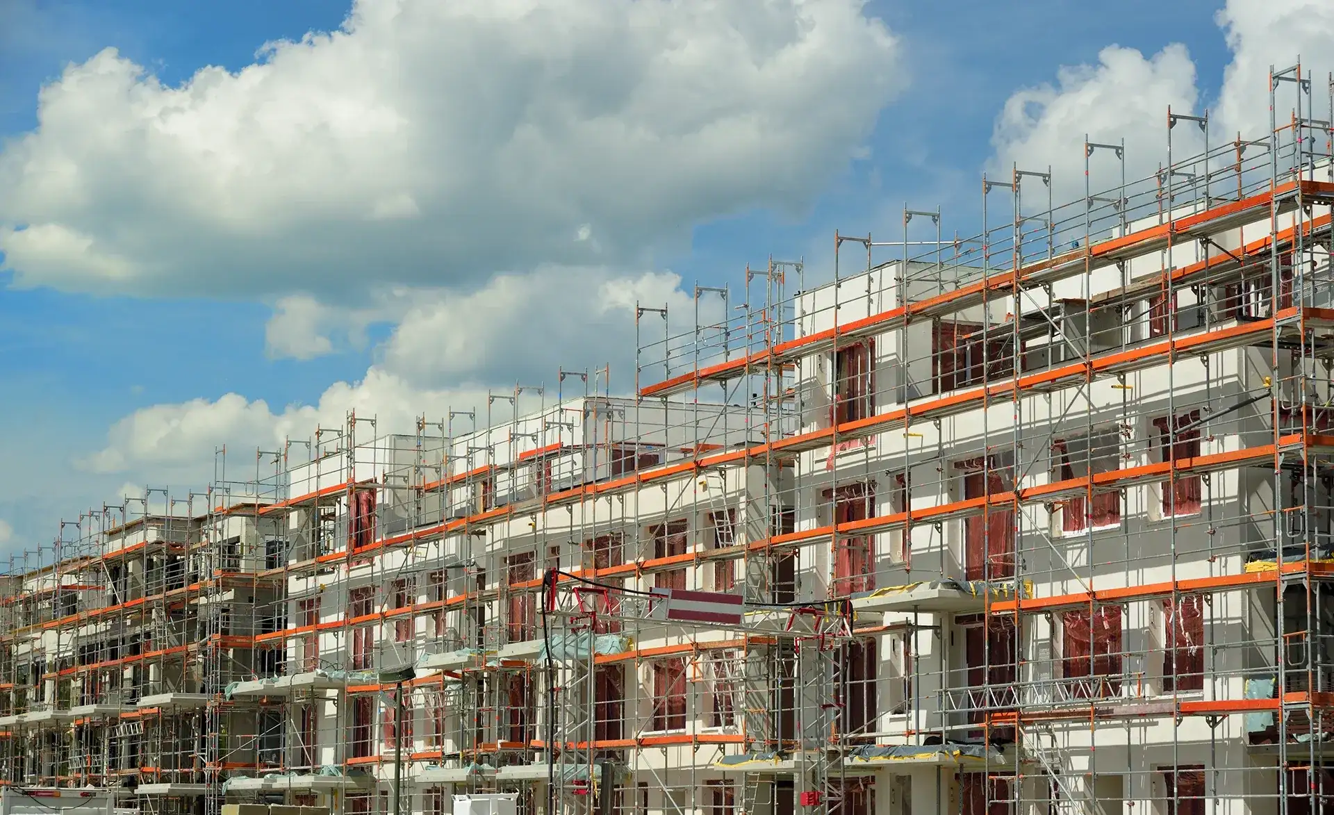 Große mehrstöckige Wohngebäude im Bauzustand, umgeben von Gerüsten vor blauem Himmel.