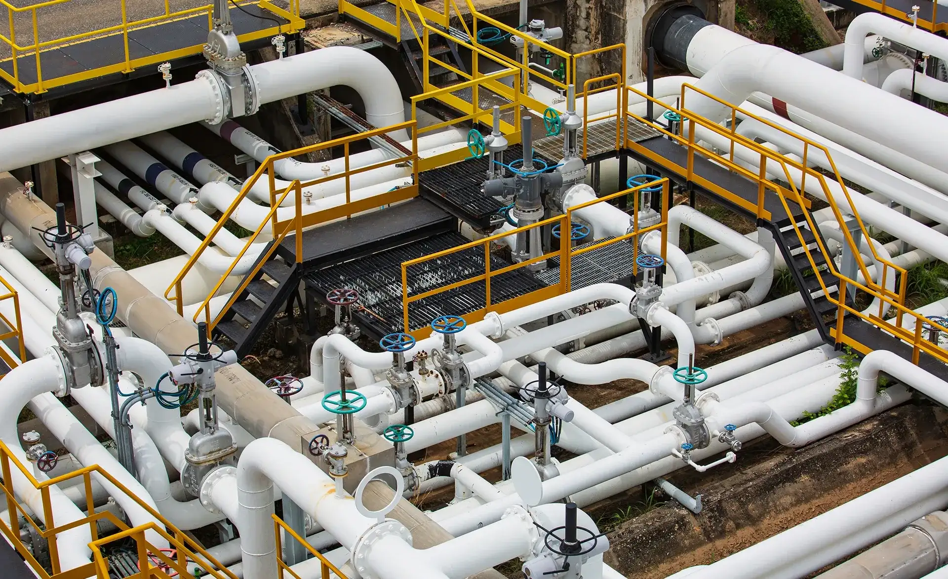 Komplexes Rohrleitungssystem mit weißen Rohren, Ventilen und gelben Wartungsstegen in einer Industrieanlage.